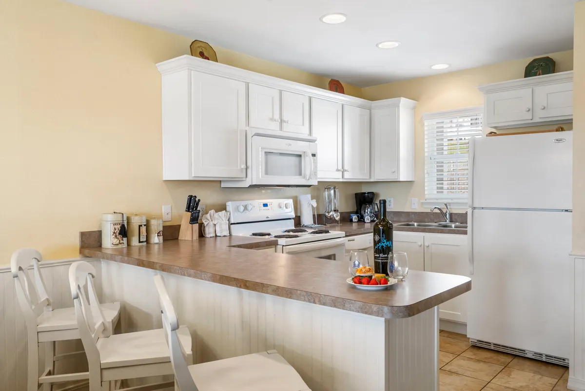A cheerful, inviting kitchen scene with a kitchen island, wine bottle and glasses, and a plate of fresh strawberries. White cabinetry and bright lighting create a welcoming space ideal for both daily meals and special occasions.