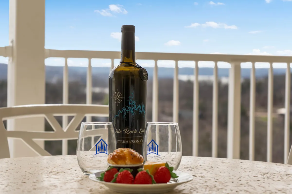 An outdoor table set with a bottle of wine, glasses, a dessert plate with strawberries and a muffin, against a backdrop of lush greenery. The setting suggests an intimate moment for couples or friends to relax, share stories, and enjoy the outdoors together.