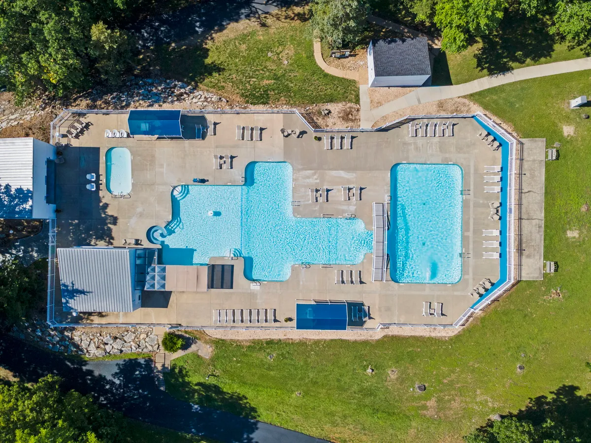 A spacious outdoor swimming pool lined with lounge chairs and shaded by cabanas, nestled amidst mature greenery. The setting invites relaxation and social gatherings, and hints at both energetic play and tranquil poolside lounging.