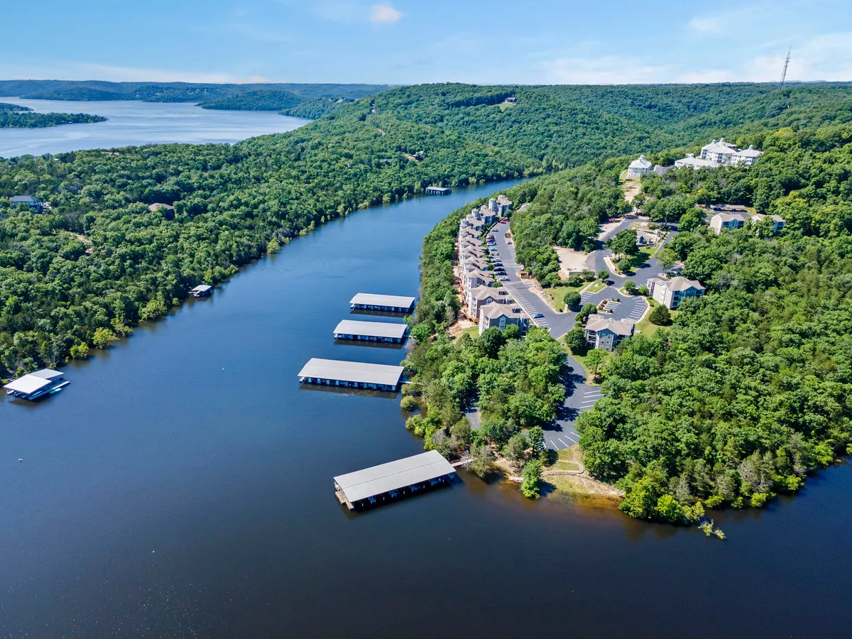 A serene view of the lake featuring a river, boathouses, residential buildings, and lush greenery. The dock area provides access to the lake, perfect for boating or fishing, while the tranquil water reflects the surrounding nature.