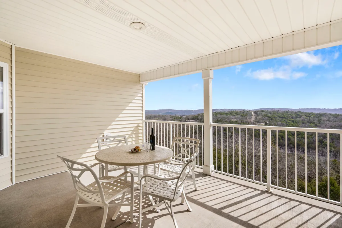 A round table and chairs are set on a deck with a bottle of wine, overlooking peaceful, scenic surroundings. The deck is an ideal spot for unwinding after outdoor adventures, with direct access to nature.