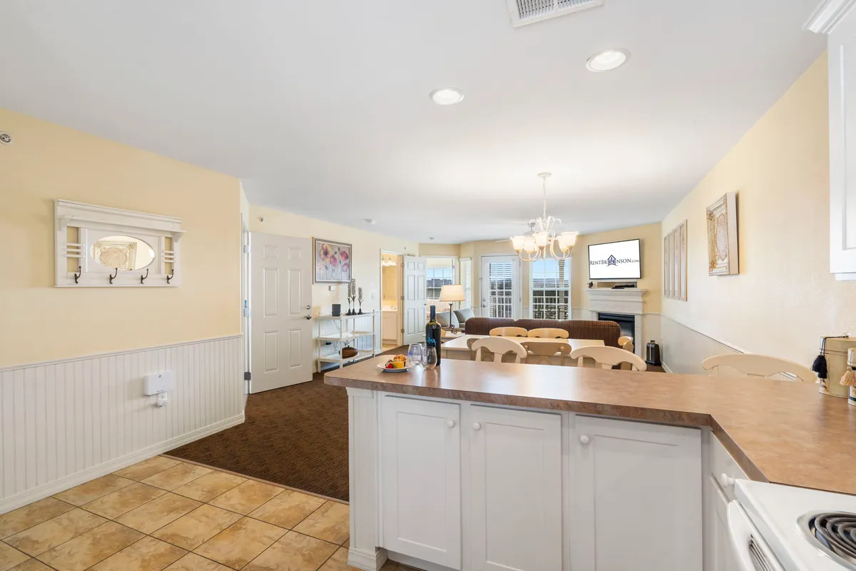 This image showcases the main living area with an open layout: a kitchen island, chandelier, dining area, and a sofa. The space is bright, inviting, and offers plenty of room for families and their pets to relax together.