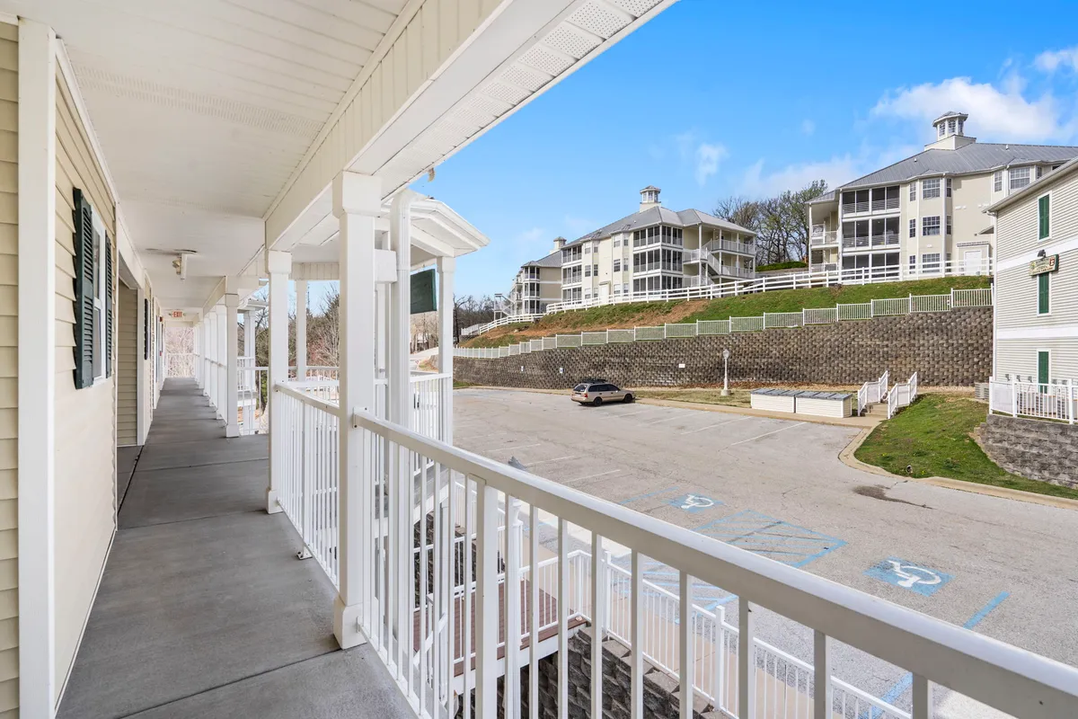 A balcony scene overlooking neighboring buildings and a roadway, set against a backdrop of soft evening light. The balcony's railing invites guests to enjoy fresh air and the company of loved ones.