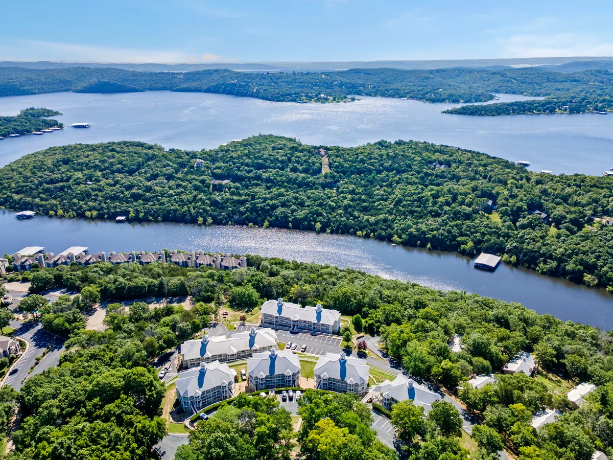 A tranquil view of the lake and surrounding greenery, with nearby buildings and a winding river visible. The calm waters suggest opportunities for boating, fishing, and relaxing, while the proximity of residential buildings hints at the convenience of stepping straight from home to lake activities.