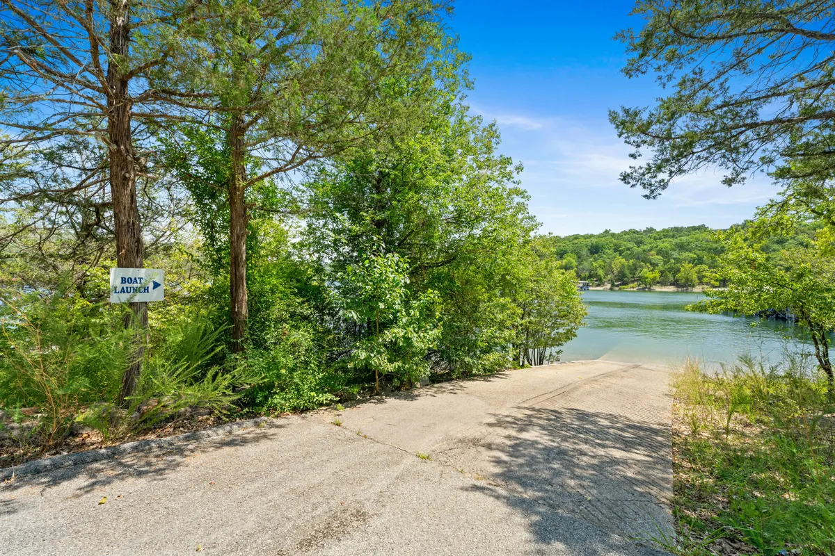 A peaceful lakeside scene with a clear view of a concrete boat ramp, a sign marking the launch area, calm water, and surrounding trees. The space is ideal for boating, fishing, or simply taking in the tranquil lakeshore.