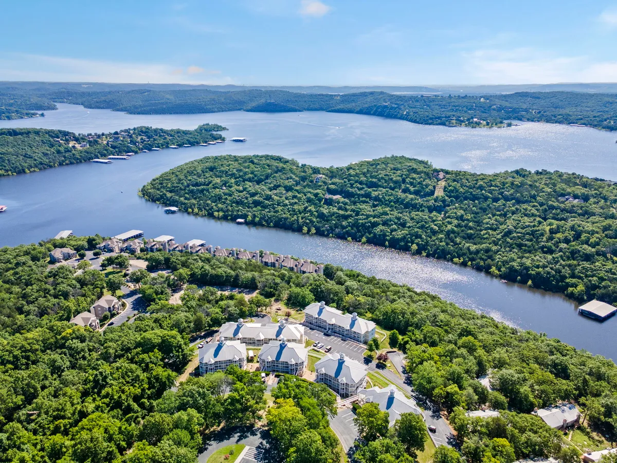 A wide view of the resort's natural surroundings, including a flowing river, forested areas, an island, and glimpses of residential accommodations. The scene is tranquil, with hints of boating and relaxing by the water, evoking a sense of adventure and space.